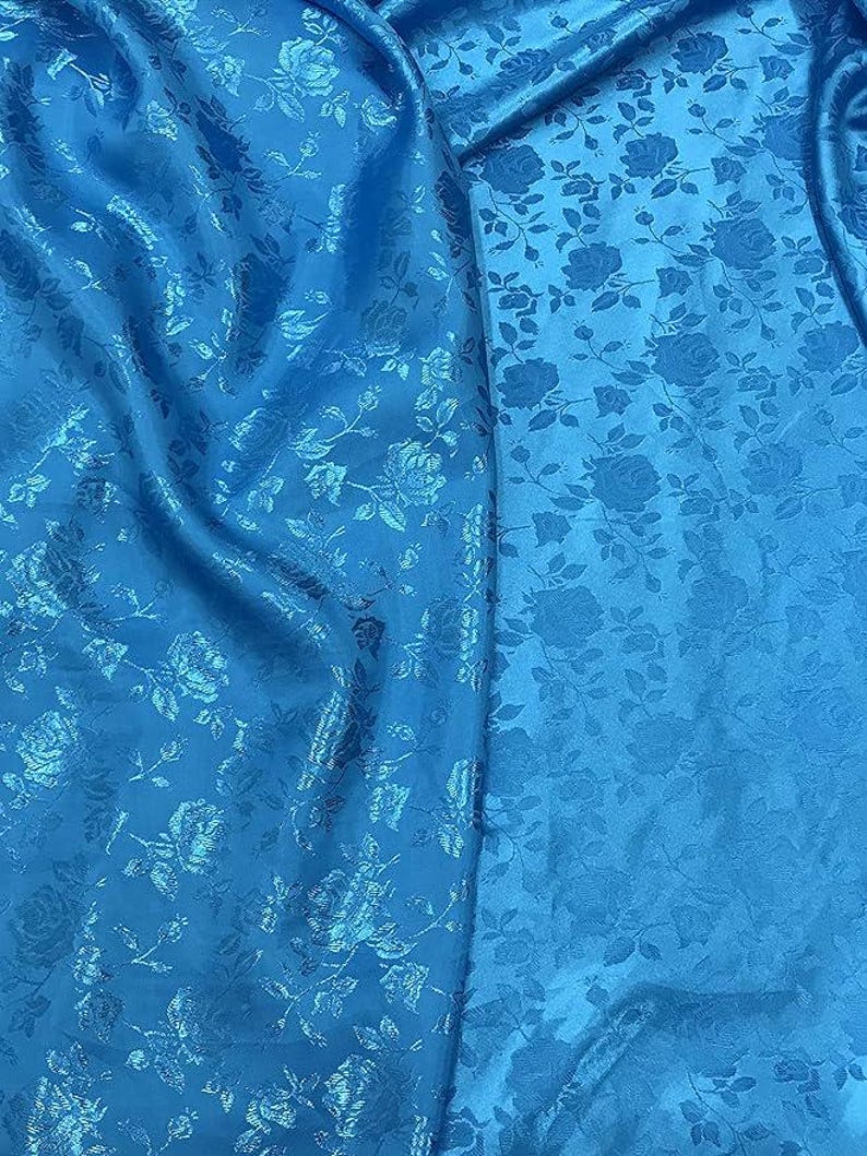 May include: Bright blue fabric with a floral rose pattern. The fabric has a slight sheen and is draped, showing the texture and design. The roses are subtly embossed, adding depth to the textile.