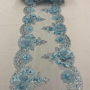 May include: Light blue floral lace trim with 3D fabric flowers, sequins, and pearl accents. The trim features a scalloped edge and is ideal for embellishing garments, accessories, or home decor projects. The trim is approximately 3 inches wide.