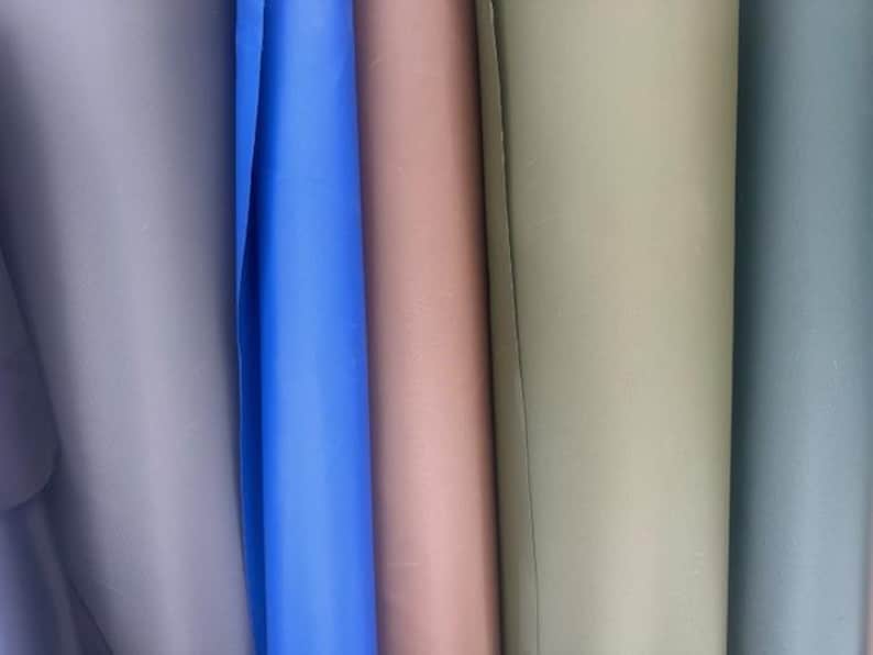 May include: A collection of five vertical rolls of smooth, matte material displayed side-by-side. The colors from left to right are a muted lavender, a vibrant royal blue, a soft dusty rose, a neutral beige, and a cool slate gray.