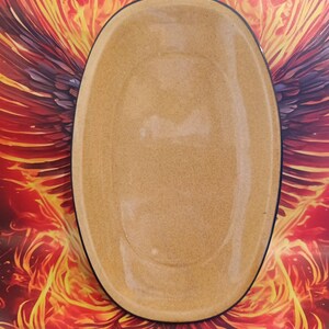 Może przedstawiać: Owalny, beżowy ceramiczny talerz do serwowania z czarną obwódką. Pusty talerz jest wyśrodkowany na tle żywego tła z czerwonych, pomarańczowych i żółtych płomieni.