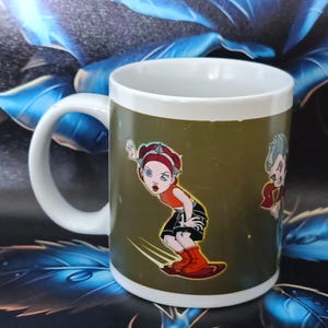 Puede incluir: Taza de café de cerámica blanca con un diseño de dibujos animados. El diseño presenta un personaje de dibujos animados con una parte superior naranja, pantalones cortos negros y botas rojas. La taza tiene un asa blanca y un fondo verde.