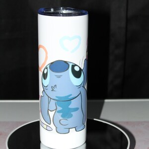 Pu&ograve; includere: Un bicchiere in acciaio inossidabile bianco con un personaggio Stitch blu di Lilo & Stitch. Il personaggio &egrave; disegnato in stile cartone animato e tiene una matita rosa. Lo sfondo &egrave; bianco con cuori e cerchi colorati.