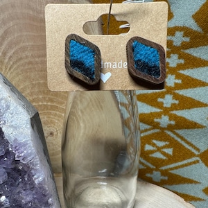 May include: A pair of handmade earrings with a diamond shape. The earrings are made of wood and have a turquoise blue fabric inlay. The earrings are displayed on a card with the word "handmade" written on it.