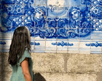 May include: A light green dress with a subtle textured pattern worn by a person standing before a blue and white tiled wall. The tiles feature intricate floral motifs, human faces, and the text A discussão de Sta Catharina in blue ink.