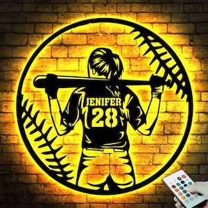 May include: A yellow illuminated baseball-shaped sign with a silhouette of a baseball player holding a bat. The player is wearing a jersey with the name "Jenifer" and the number "28".
