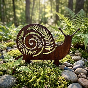 Könnte beinhalten: Eine rostfarbene Metall-Gartenskulptur in Form einer Schnecke. Das Schneckenhaus weist ein detailliertes Ausschnittmuster aus Farnwedeln auf. Die Skulptur verfügt über zwei kleine Metallspieße an der Basis zur Befestigung im Boden.