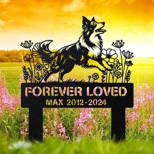 May include: Black metal garden stake with a running dog silhouette, the words "FOREVER LOVED" and "MAX 2012-2024". The dog is black and white, with floral accents. The stake is in a garden with pink flowers and a yellow sky.