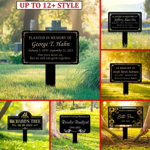 May include: Black memorial garden stakes with white text, including names, dates, and phrases such as "In Loving Memory" and "Our lives move on." The stakes have decorative borders and are placed in a grassy area. The text is in white.