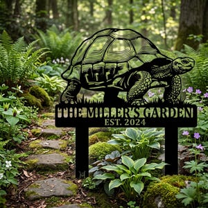 Op de afbeelding: Een zwart metalen tuinbord met een gedetailleerd silhouet van een schildpad. Onder de schildpad staat de tekst THE MILLER'S GARDEN en EST. 2024. Het bord wordt ondersteund door twee verticale palen die in de grond gestoken kunnen worden.