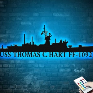 May include: A blue neon sign with a silhouette of a ship and the text "USS THOMAS C. HART FF-1092".