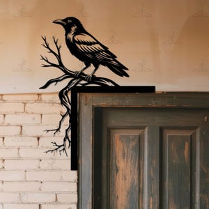 May include: Black metal raven perched on a branch, designed for wall decor. The raven is detailed with feathers and sits on a branch with several twigs. The artwork is mounted on a corner, with a brick wall and a wooden door in the background.