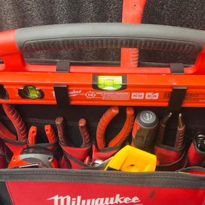 May include: A red and black Milwaukee tool bag filled with various hand tools. The bag features a level, pliers, screwdrivers, and other tools. The bag has a black handle and a red interior.