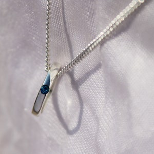 May include: A silver necklace with a small, round pendant featuring a blue gemstone.