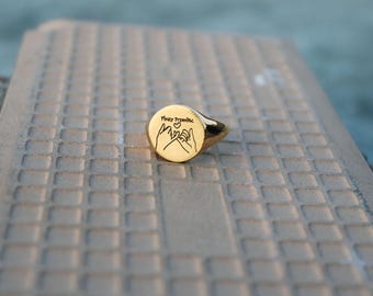 May include: A gold signet ring with a pinky promise design and the words "Pinky Promise" engraved on the face.