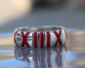 May include: A silver ring with red enamel detailing. The ring features the Roman numeral 'XIII' in red enamel.