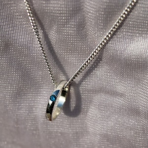 May include: A silver chain necklace with a silver ring pendant featuring a small blue gemstone.