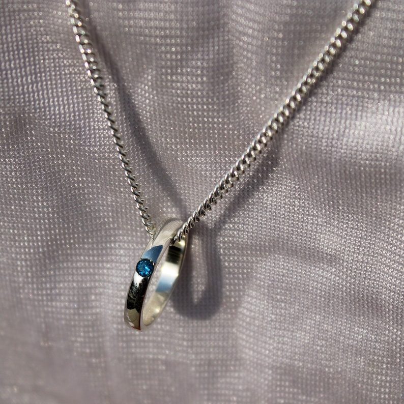 May include: A silver chain necklace with a silver ring pendant featuring a small blue gemstone.