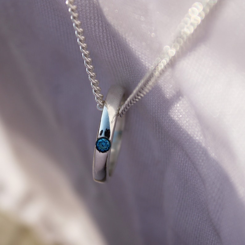May include: A silver necklace with a small blue gemstone pendant. The pendant is a simple ring with a single stone set in the center.