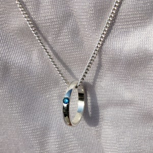 May include: A silver chain necklace with a silver ring pendant featuring a small blue gemstone.