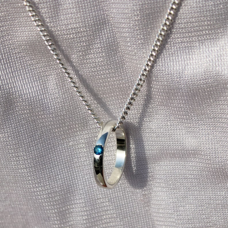 May include: A silver chain necklace with a silver ring pendant featuring a small blue gemstone.