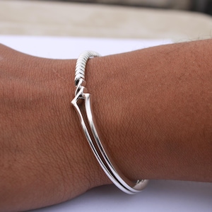 May include: A silver bangle bracelet with a twisted design. The bracelet is open and has a hinged clasp.