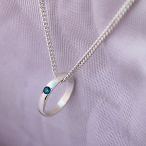 May include: A silver chain necklace with a silver ring pendant featuring a small blue gemstone.