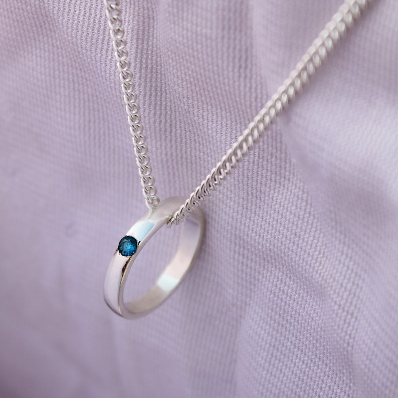 May include: A silver chain necklace with a silver ring pendant featuring a small blue gemstone.