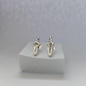 May include: A pair of silver earrings with a dagger design. The earrings are on a white surface.
