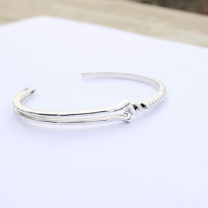 May include: A silver bangle bracelet with a twisted design. The bracelet is open and has a simple, elegant style.