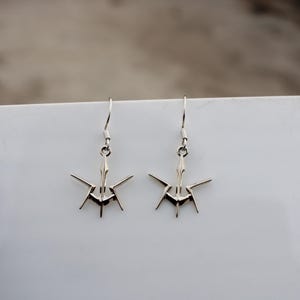 Pode incluir: Um par de brincos de prata com um design geométrico. Os brincos são feitos de metal e têm uma forma afiada e angular.