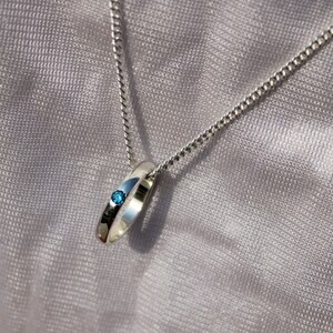 May include: A silver chain necklace with a silver ring pendant featuring a small blue gemstone.
