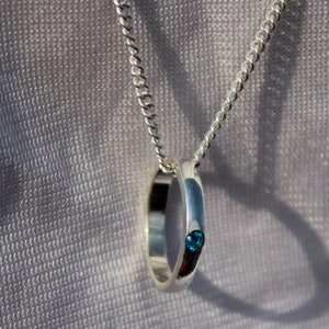 May include: A silver chain necklace with a silver ring pendant featuring a small blue gemstone.