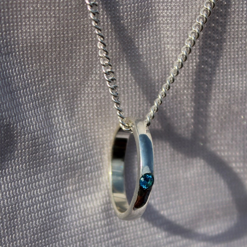 May include: A silver chain necklace with a silver ring pendant featuring a small blue gemstone.