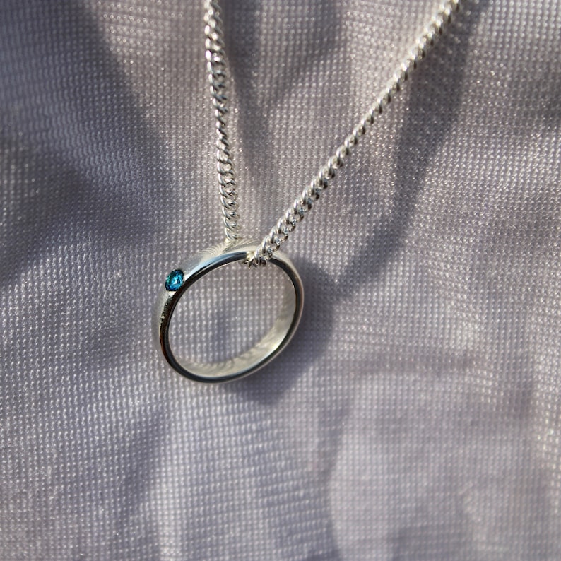 May include: A silver chain necklace with a silver ring pendant featuring a small blue gemstone.