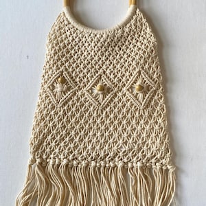 May include: A beige crocheted tote bag with wooden handles and wooden beads. The bag has a fringe detail at the bottom.