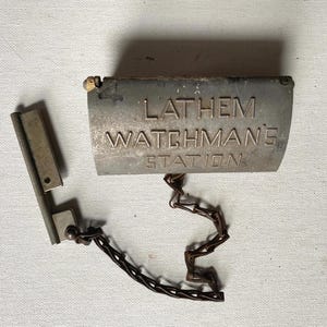 May include: A vintage metal watchman's station with a chain attached. The station is labeled "Lathem Watchman's Station".