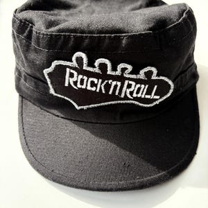 May include: Black cotton cap with a white embroidered patch that says "Rock 'n' Roll" with a stylized hand gesture.