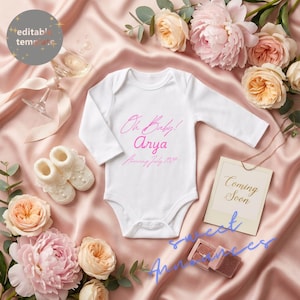 May include: A white baby onesie with the text "Oh Baby! Arya, Arriving July 2024" in pink script. The image includes baby booties, flowers, and a "Coming Soon" card, all arranged on a pink satin surface.