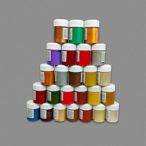 Könnte beinhalten: Eine Pyramide aus 24 kleinen Farbtöpfen mit weißen Deckeln. Die Töpfe sind in Pyramidenform angeordnet, wobei der kleinste Topf oben und die größten Töpfe unten liegen. Die Töpfe sind mit verschiedenen Farben gefüllt, darunter Gold, Silber, Rot, Grün, Blau und Lila.