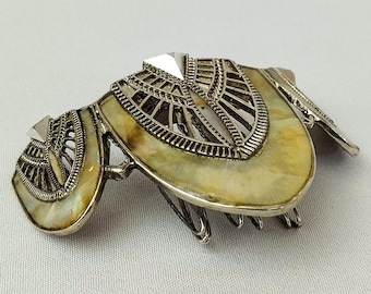 May include: A silver-toned hair comb featuring three distinct sections with intricate metal filigree overlays. Each section contains a smooth, marbled, cream and yellow-toned inlay. The comb has multiple metal teeth extending from the base.