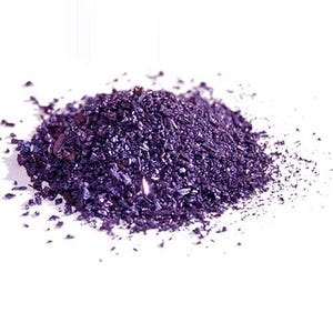 Può includere: Un piccolo mucchio concentrato di granuli cristallini viola intenso con una lucentezza metallica e riflettente. Le singole particelle variano per dimensioni e forma, creando un aspetto strutturato e frastagliato che cattura la luce.