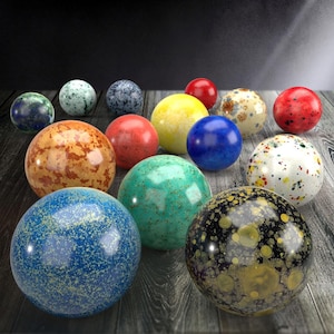 Può includere: Una collezione di quindici oggetti sferici di vari colori e texture, tra cui rosso solido, giallo brillante, blu intenso e motivi maculati multicolori. Le sfere hanno una finitura liscia e lucida e sono disposte in un gruppo.