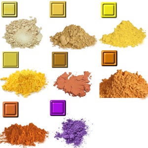 May include: A collection of nine piles of colorful powder pigments, including shades of beige, brown, yellow, orange, and purple. Each pile is accompanied by a square, metallic-looking tile in a matching color. The powders appear finely ground.