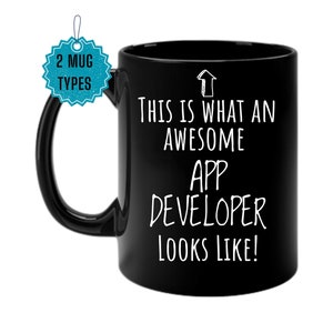 May include: Black coffee mug with white text that reads "This is what an awesome app developer looks like!"  The mug has a white arrow pointing upwards.