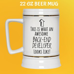Op de afbeelding: Witte 650 ml bierpul met gouden rand en een handvat. De pul heeft de zwarte tekst "THIS IS WHAT AN AWESOME BACK-END DEVELOPER LOOKS LIKE!". De tekst "22 OZ BEER MUG" staat bovenaan.