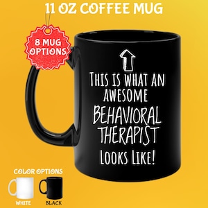 May include: Black 325 ml coffee mug with the text "THIS IS WHAT AN AWESOME BEHAVIORAL THERAPIST LOOKS LIKE!" in white. The mug has a black handle and the words "8 MUG OPTIONS" are on a red tag. Color options are white and black.
