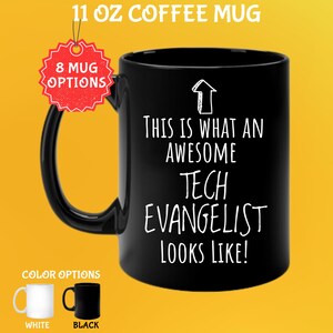 Könnte beinhalten: Eine schwarze 325 ml Kaffeetasse mit dem weißen Text "THIS IS WHAT AN AWESOME TECH EVANGELIST LOOKS LIKE!". Die Tasse hat einen schwarzen Henkel und wird mit weißen und schwarzen Farboptionen gezeigt.