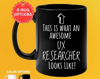 May include: Black 11 oz coffee mug with the text "THIS IS WHAT AN AWESOME UX RESEARCHER LOOKS LIKE!" in white. The mug has a black handle and is shown with white and black color options. The mug has a tag that says "8 MUG OPTIONS".