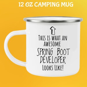 May include: White 12 oz camping mug with a silver rim and handle. The mug features the text "THIS IS WHAT AN AWESOME SPRING BOOT DEVELOPER LOOKS LIKE!" in black. The words "12 OZ CAMPING MUG" are at the top.