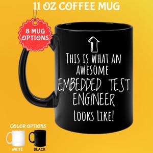 Op de afbeelding: Zwarte koffiemok van 325 ml met de witte tekst "THIS IS WHAT AN AWESOME EMBEDDED TEST ENGINEER LOOKS LIKE!". De mok heeft een zwart oor en een rood label met "8 MUG OPTIONS". Kleuropties zijn wit en zwart.